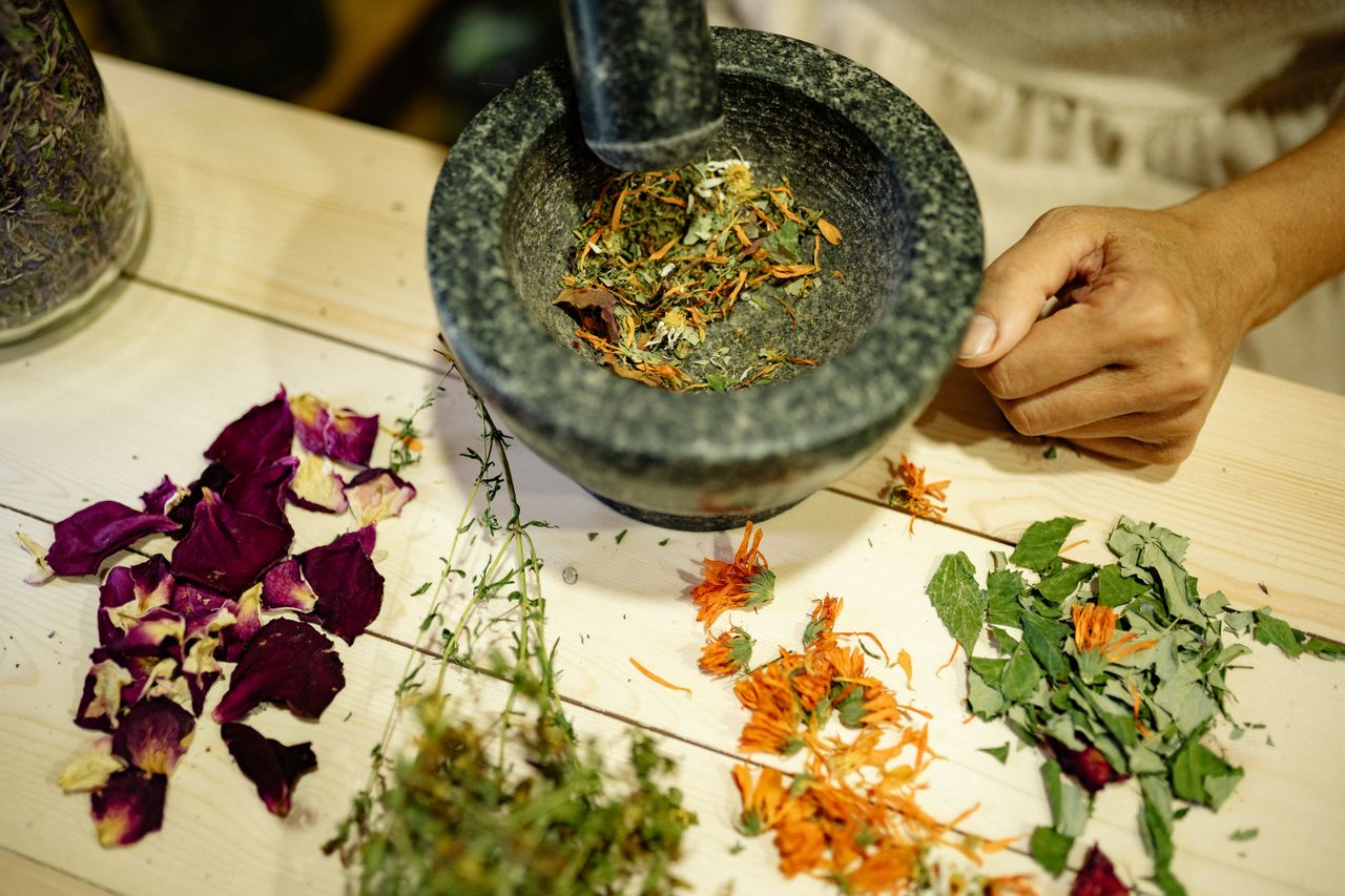 services-04 A detailed view of herbs and flower petals being ground in mortar and pestle on wooden table.