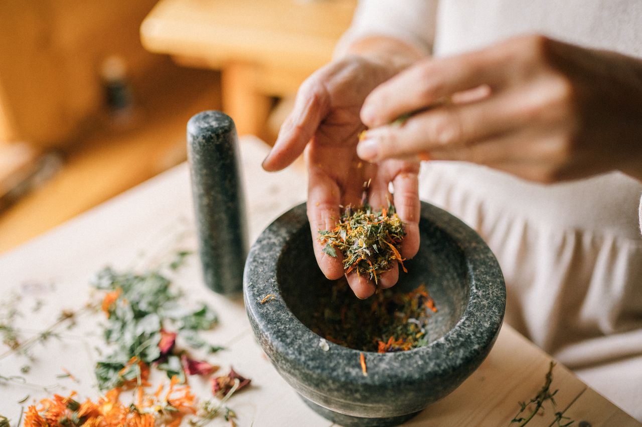 services-03 A woman uses a mortar and pestle to crush dried herbs for traditional medicine preparation.