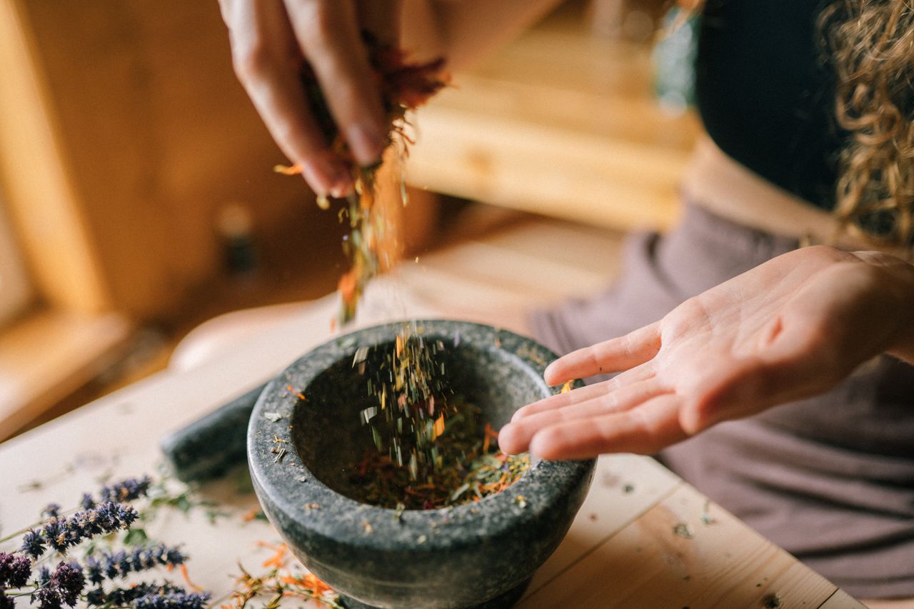 about-us-01 A person preparing dried herbs using a mortar and pestle on a wooden table, seen from above.